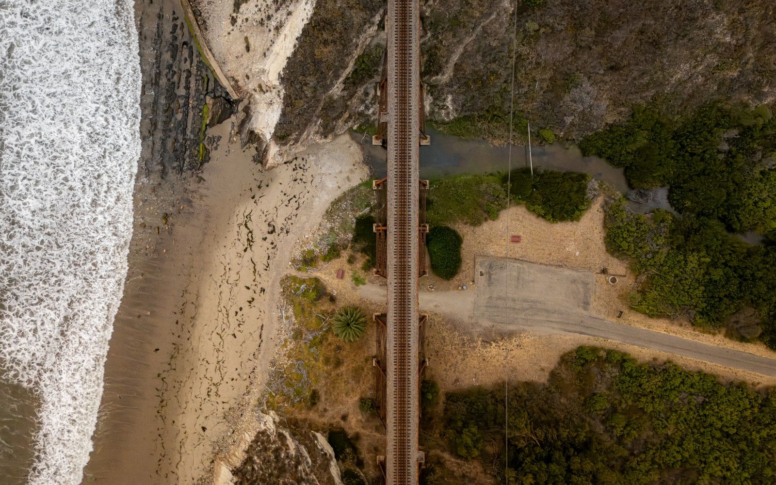 Aerial view of a railway trestle bridge crossing a stream near a sandy beach