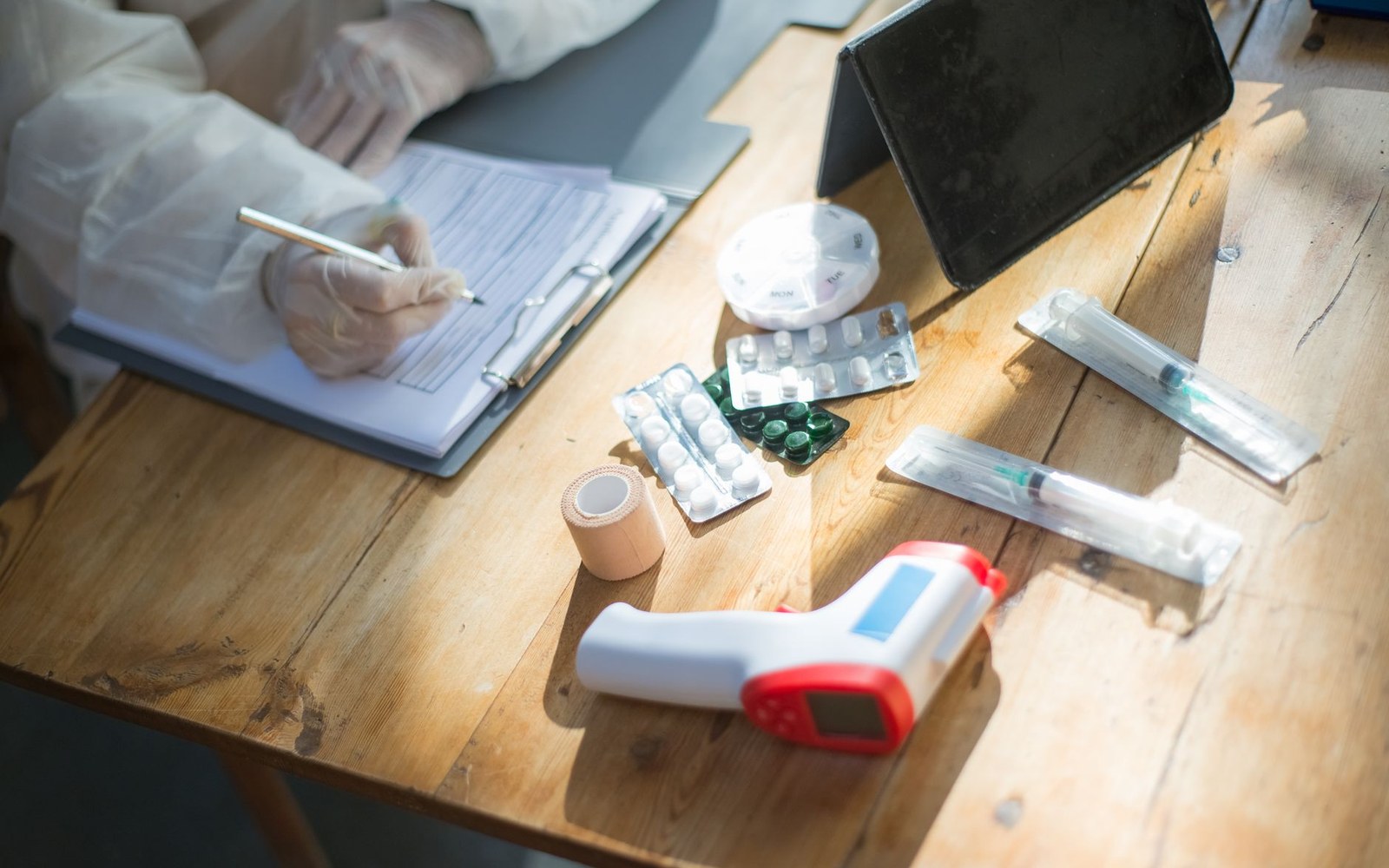 Gloved worker fills out a form beside syringes, pill packets, tape and a thermometer