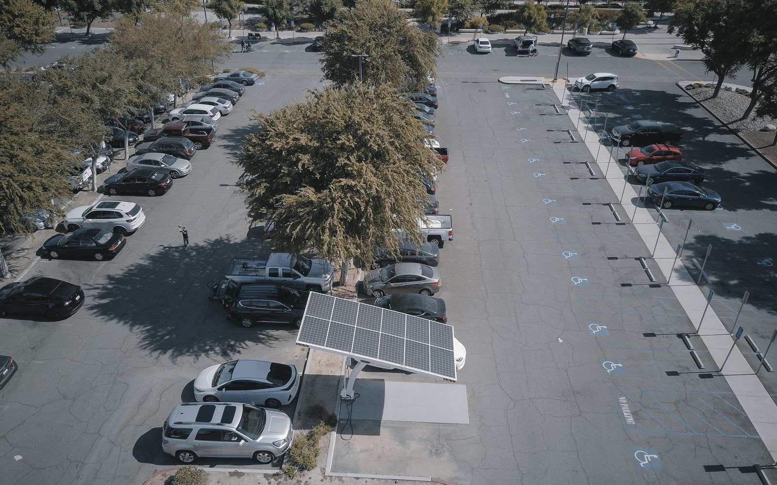 Aerial view of a parking lot with a solar carport charging station among rows of vehicles