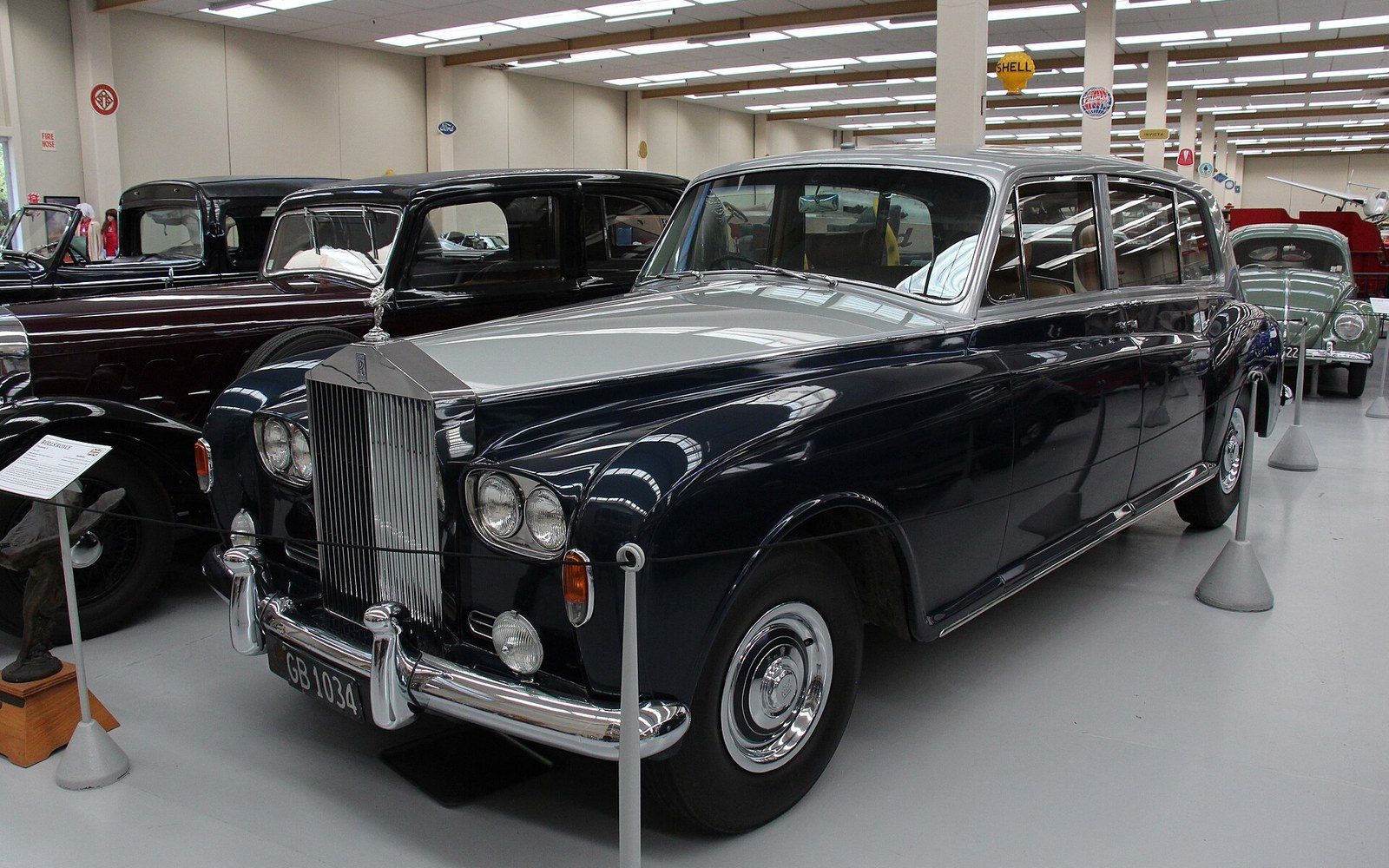 A vintage dark blue Rolls-Royce limousine on display among classic cars in a museum