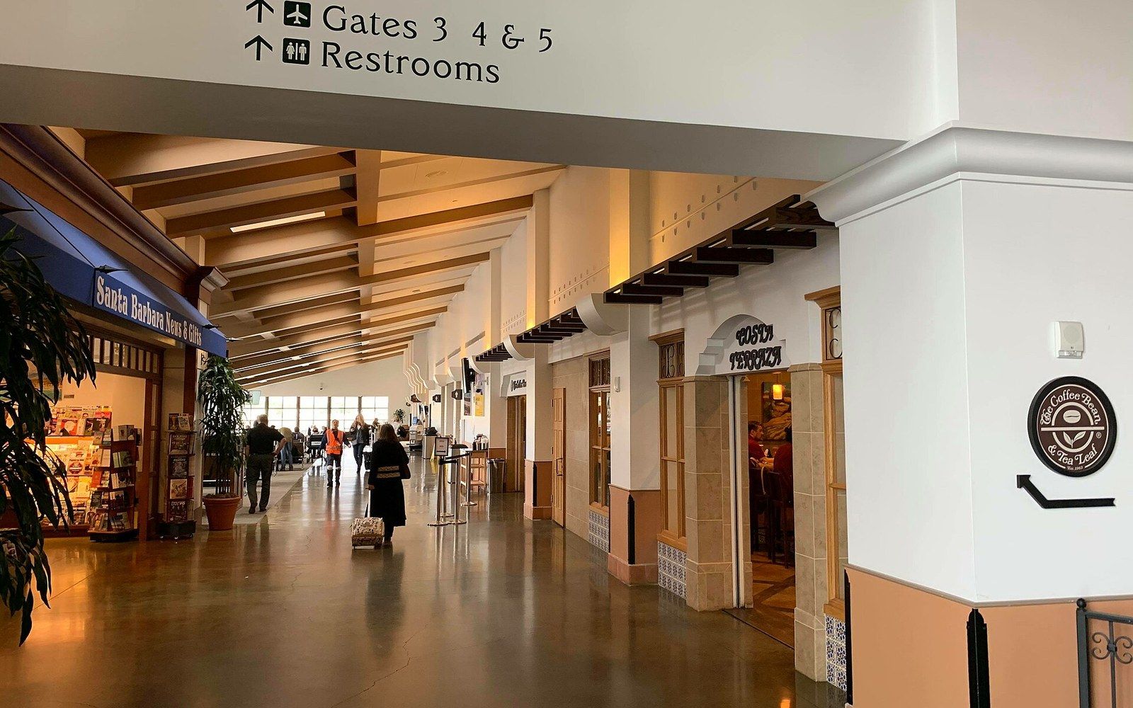 Airport terminal corridor with shops, signage for gates and restrooms overhead