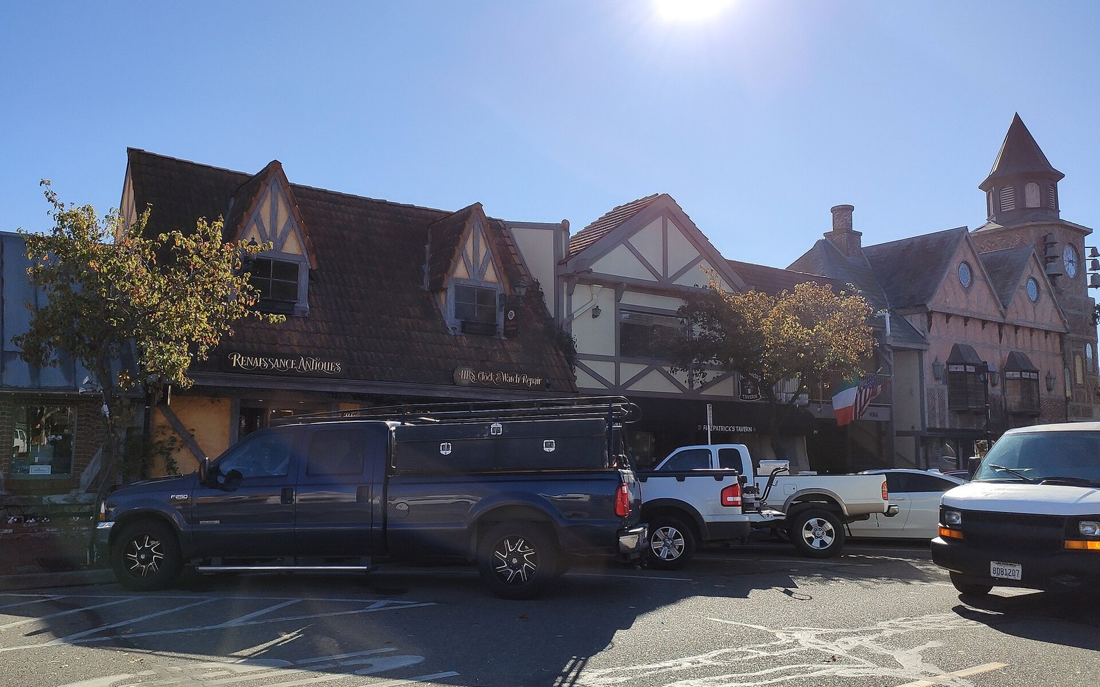 Pickup trucks parked outside Tudor-style shops with steep gabled roofs and a clock tower