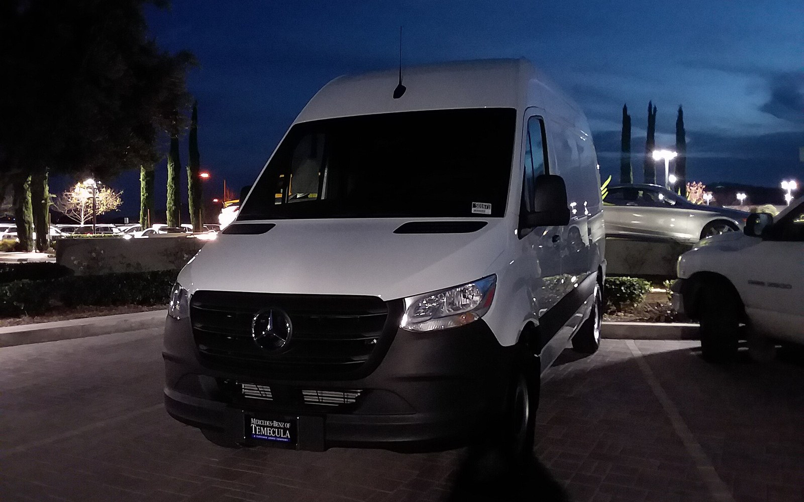 White Mercedes-Benz Sprinter high-roof cargo van parked in a dealership lot at dusk